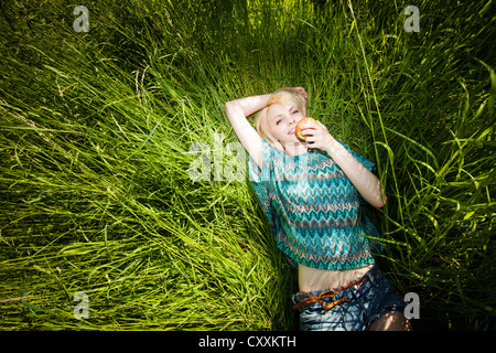 Lächelnde junge Frau in hohe Gräser hält einen Apfel liegen Stockfoto