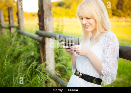 Junge Frau lehnt sich an einen Zaun, der die Kommunikation per Handy, smartphone Stockfoto