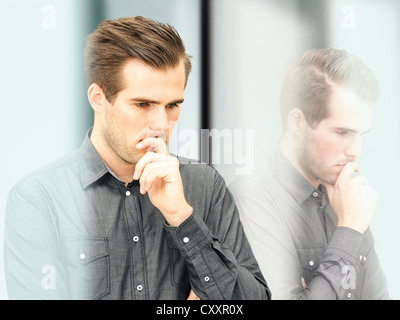 Nachdenklicher junger Geschäftsmann steht man vor einer Glasscheibe mit Reflexion Stockfoto