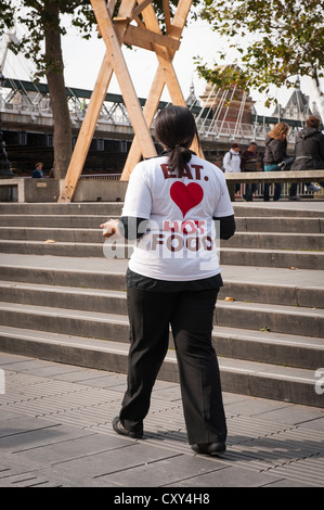 Londoner Southbank Essen, hübsche junge Frau schwarz Kellnerin Pferdeschwanz Hände Verkoster an Passanten durch T-shirt Liebe Herz heißes Essen Stockfoto