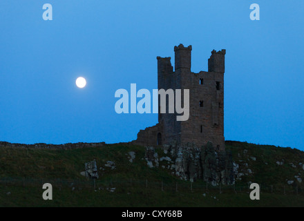 Dunstanburgh Castle, Northumberland, England in der Dämmerung mit dem Mond hinter. Stockfoto