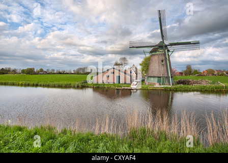 Eine typische holländische Windmühle auf einem Bauernhof durch einen Kanal an einem bewölkten Tag Stockfoto