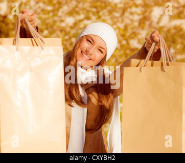 Foto von niedlichen fröhliches Mädchen mit Einkaufstüten, Closeup Portrait der hübsche Frau im Herbst Laub Hintergrund isoliert Stockfoto