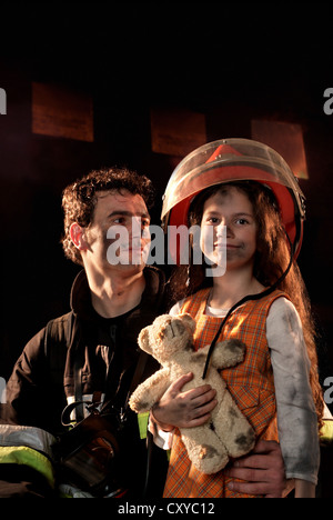 Feuerwehrmann mit einem Mädchen, die er aus einem brennenden Haus gerettet Stockfoto