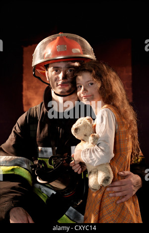 Feuerwehrmann mit einem Mädchen, die er aus einem brennenden Haus gerettet Stockfoto