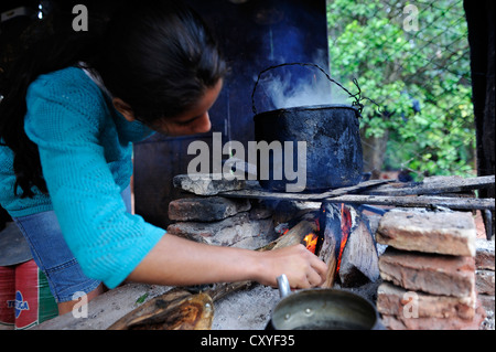 Junge Frau, die Kochen über dem offenen Feuer in der einfachen Küche der Landarbeiter, Comunidad Arroyito, Departamento Concepcion Stockfoto