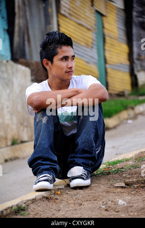 Teenager, 16 Jahre alt, sitzt am Straßenrand vor Wellblechhütten, Lomas de Santa Faz Slum, Guatemala-Stadt Stockfoto