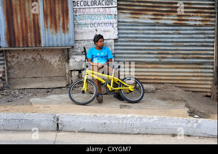 Teenager mit einem gelben Fahrrad sitzen boredly vor einer Hütte, Lomas de Santa Faz Slum, Guatemala-Stadt, Guatemala Stockfoto