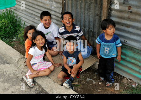 Lächelnde Kinder sitzen vor einer Wellpappe-Eisen-Hütte, Lomas de Santa Faz Slum, Guatemala City, Guatemala, Mittelamerika Stockfoto