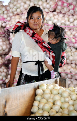 Indigene Frau, die trägt eines kleinen Mädchens in einem Tragetuch vor Säcke mit Zwiebeln, CENMA, Gemüse Großmarkt in der Stockfoto