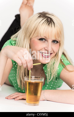 Junge Frau auf dem Boden mit einem Glas Apfelsaft mit einem Trinkhalm vor ihr liegend Stockfoto