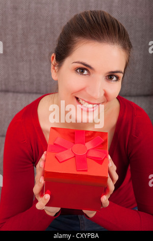 Schöne und glückliche Frau auf dem Sofa hält ein Weihnachtsgeschenk Stockfoto