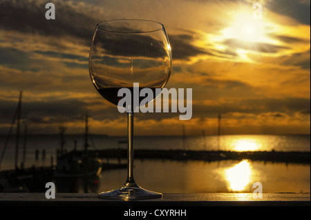 Glas Rotwein auf der Schiene von einem Balkon bei Sonnenuntergang mit Blick auf den Hafen, Timmendorf, Mecklenburg-Vorpommern Stockfoto