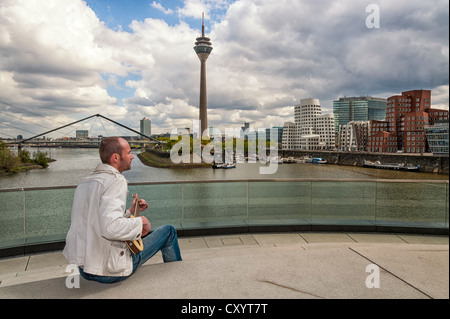 Junger Mann, sitzend mit einer Gitarre im Hafen von Düsseldorf, Nordrhein-Westfalen Stockfoto