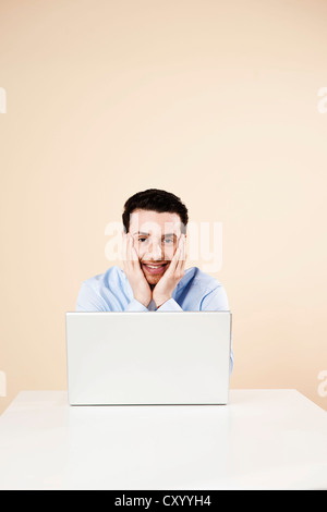 Junger Mann vor seinem Laptop sitzt lächelnd Stockfoto