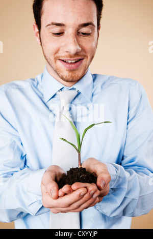 Lächelnde junge Manager, die eine Pflanze in den Händen hält Stockfoto
