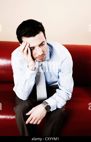 Junger Mann nachdenklich auf dem Sofa sitzen und warten Stockfoto