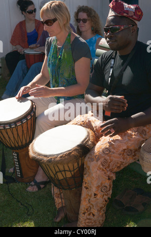 Schwarzer Mann und eine weiße Frau, die afrikanische Trommeln zu spielen. Er lehrt sie, zu spielen. Stockfoto