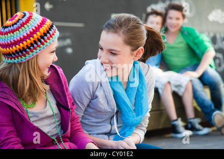 Zwei Girls chattest, zwei Jungs sitzen auf der Rückseite Stockfoto