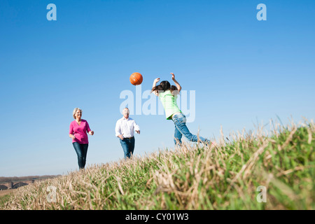 Mädchen spielen Ball mit ihren Großeltern auf einer Wiese Stockfoto