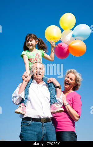 Großeltern, die ihre Enkelin zu halten, während sie farbige Luftballons in der Hand hält Stockfoto