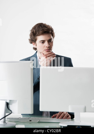 Junge Manager auf zwei Monitoren gleichzeitig arbeiten Stockfoto