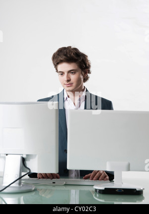 Junge Manager auf zwei Monitoren gleichzeitig arbeiten Stockfoto