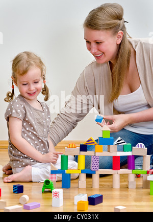 Kleine Mädchen und junge Frau, die Spaß spielen mit Bauklötzen auf dem Boden Stockfoto