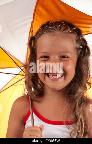 Kleines Mädchen hält Regenschirm und zeigt zwei fehlende Zähne Stockfoto