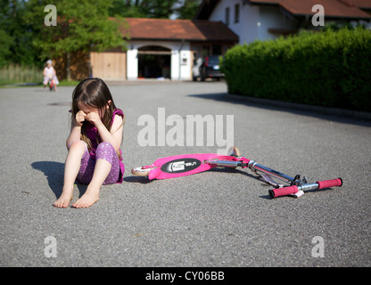 Kleines Mädchen, hat drei Jahre aus ihrem Roller, sitzen auf den Boden Weinen gefallen. Stockfoto