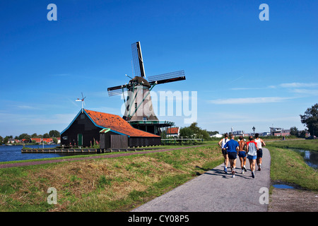 Niederlande, Nordholland, Zaanstad, Zaanse Schans, Windmühlen, Jogger am Weg entlang des Kanals. Stockfoto