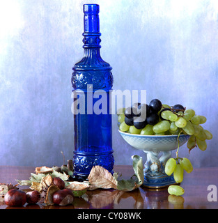 Stillleben: blaue Glasflasche mit herbstlichen Früchte, Trauben und Kastanien und Blätter auf einem Holztisch poliert Stockfoto