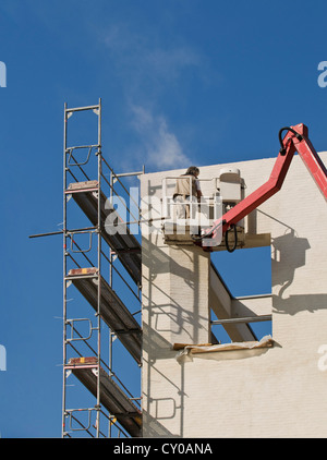 Baustelle, Arbeiter stehen auf einer erhöhten Kran-Plattform und Schleifen Gips, Arbeitssicherheit Stockfoto
