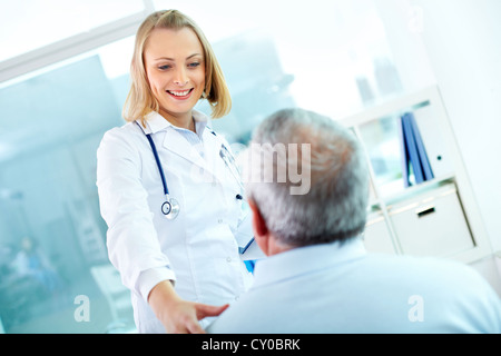 Porträt des jungen hübschen Assistenten Blick auf Reife Kliniker während der Interaktion mit ihm Stockfoto