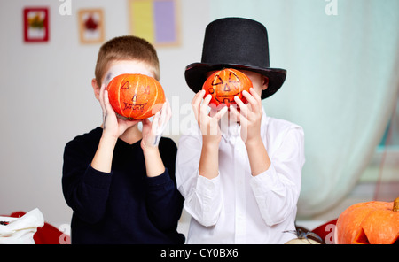 Foto von unheimlichen Zwillingen halten Halloween Kürbisse vor den Gesichtern Stockfoto