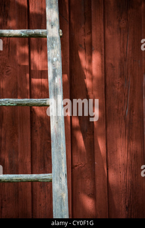 Leere Leiter lehnte sich gegen die Wand des roten Hauses Stockfoto