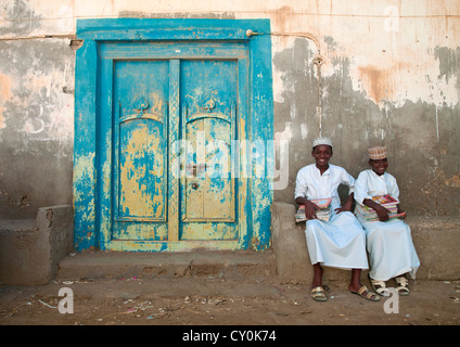 Zwei Kinder In weißen Dischdascha sitzt neben A Blau Holztür, Mirbat, Oman Stockfoto