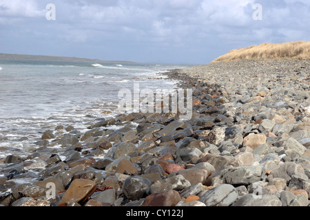 ein Kiesstrand an einem sonnigen Tag mit ruhiger Seewellen spritzt gegen die Kieselsteine als Hintergrund mit Gezeiten-Marken Stockfoto