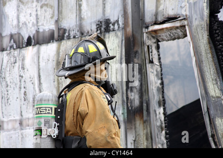 Ein Feuerwehrmann steht vor den Ruinen eines Industriebaus zusammengebrochen, die bei einem Brand Stockfoto