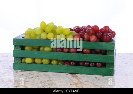 Rote und grüne Trauben in einer Holzkiste auf eine Granit-Arbeitsplatte. Querformat mit einem weißen Hintergrund. Stockfoto