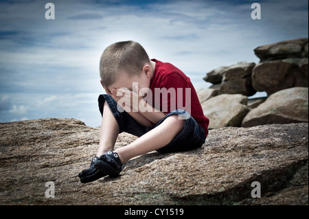 Ein fünf-jähriger Junge mit Autismus Gefühl überwältigt von seiner Umgebung verbirgt sein Gesicht in seinen Händen. Stockfoto