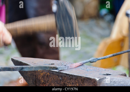 Vorschlaghammer in Motion blur zerschlägt mit volle Wirkkraft in ein glühendes Eisen Stab Werkstück auf einem Schmied Amboss Stockfoto