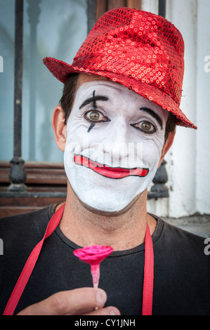 Ein Porträt von Clown Straßenkünstler in Las Palmas de Gran Canaria Spanien trägt einen roten Hut mit weißen Gesicht, die eine Blume Stockfoto