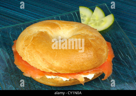 Bagel mit Frischkäse und Räucherlachs mit Gurkenscheiben auf eine transparente Platte über einen blauen Hintergrund Stockfoto