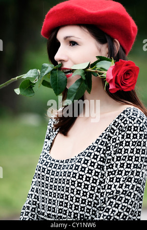 eine Frau in einem schwarzen und weißen Kleid hält, dass eine rote rose im Mund Stockfoto