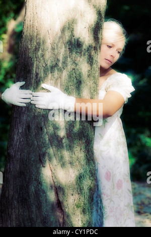 eine Frau in einem geblümten Kleid ist einen Baum umarmen. Stockfoto