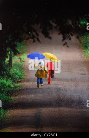 Jungen und Mädchen laufen auf Landstraße in den Regen halten bunte Sonnenschirme Stockfoto