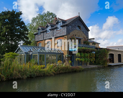 Blumenampeln zieren einen aufwendigeren Balkon auf einem schönen Haus mit einem schönen Garten mit Blick auf den Grand Union Canal. Stockfoto