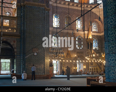 Neue Moschee Yeni Camii in Istanbul Türkei ca 1640, Interieur mit Menschen beten, warmes Licht von Kronleuchtern Stockfoto