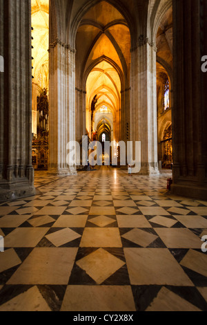 Innenansicht des beleuchteten langen Seitenkapellkorridors in der Kathedrale mit herrlichen gotischen Bögen und schwarz-weißem Marmorboden Stockfoto